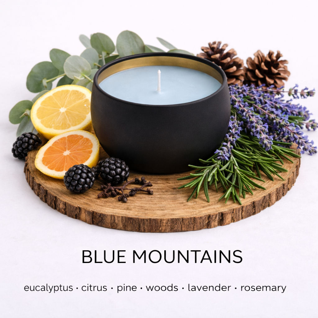 Matte black soy candle with light blue wax in a gold-lined tin, styled on a wooden base with eucalyptus leaves, citrus slices, pinecones, lavender, and rosemary to represent the Blue Mountains scent by Fair Dinkum Scents