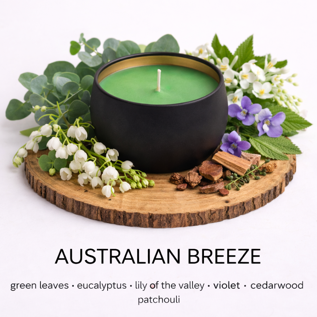 Matte black soy candle with green wax in a gold-lined tin, styled on a wooden base with eucalyptus leaves, lily of the valley, violet flowers, and cedarwood to represent the Australian Breeze scent by Fair Dinkum Scents