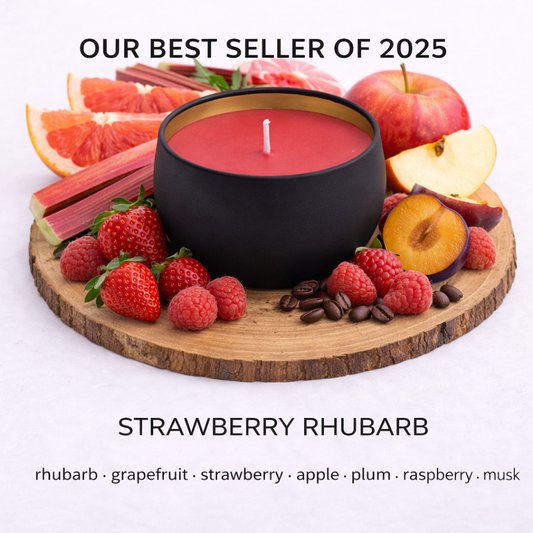 Black candle on a wooden board with fruits and berries, labeled as 'Best Seller of 2025' for strawberry rhubarb fragrance.